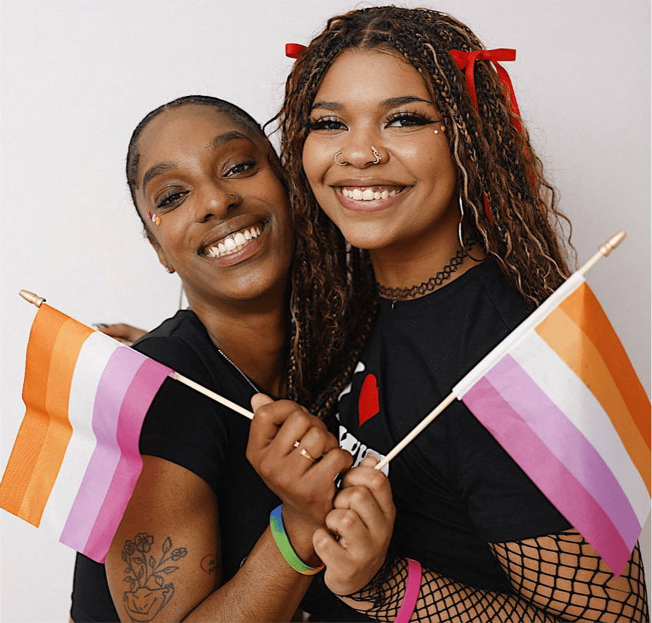 Two smiling young women embracing while holding small lesbian Pride flags.