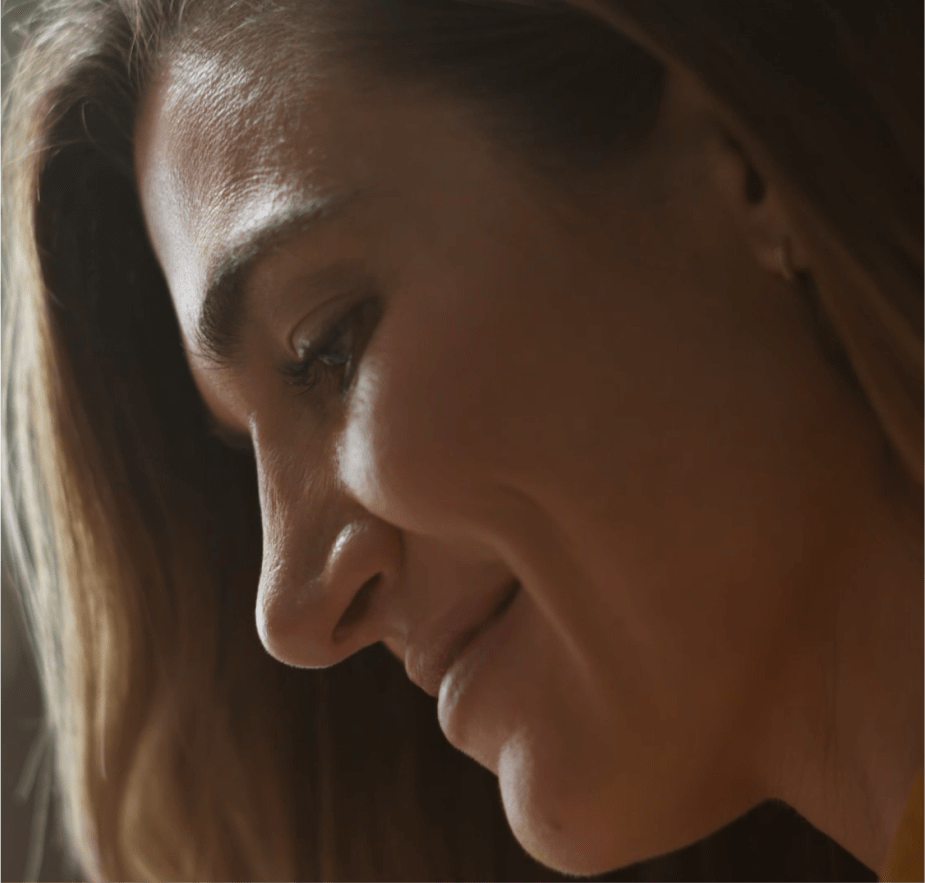 A close-up profile of a woman with long hair smiling softly in warm lighting.