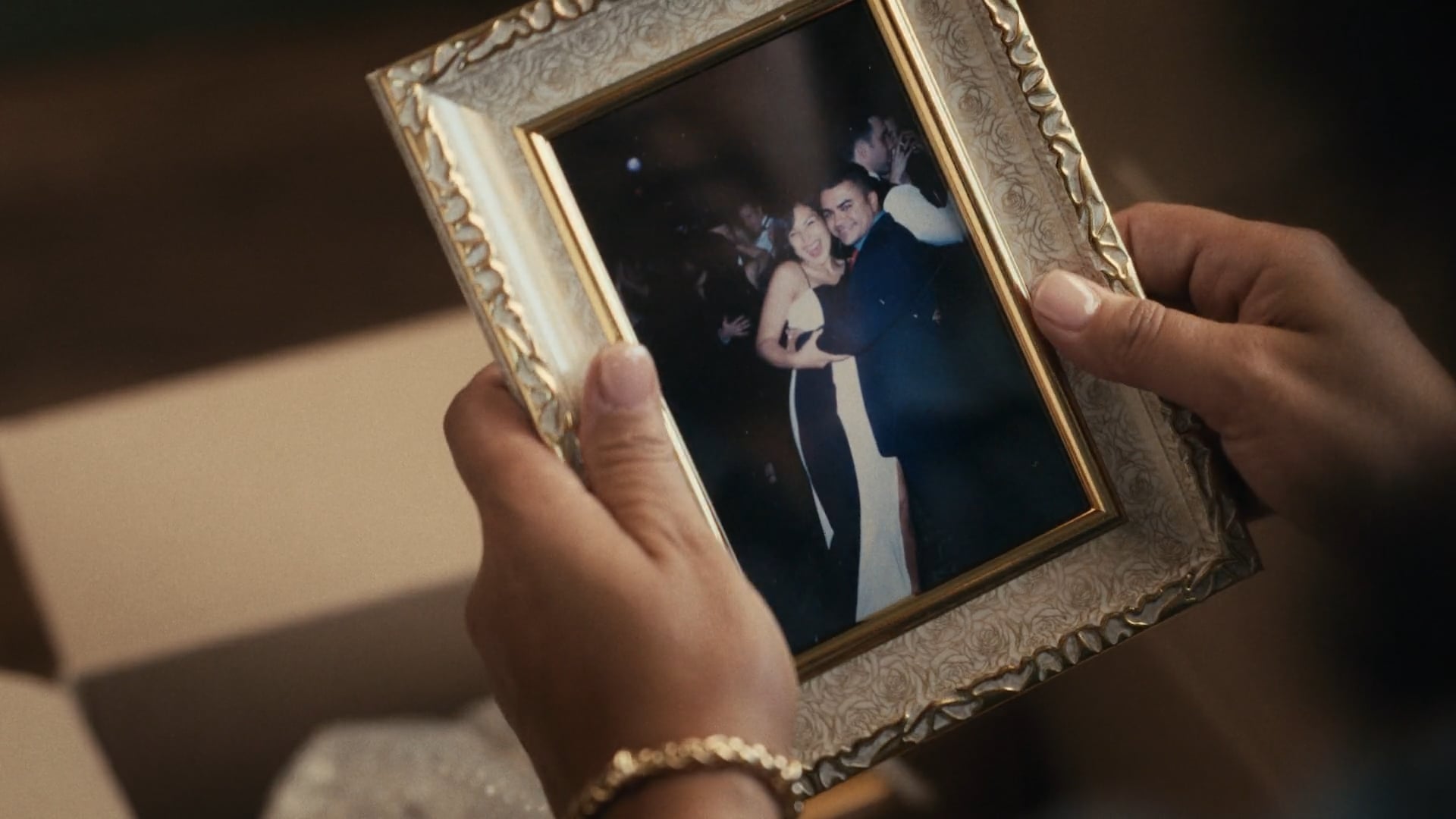 Close-up of hands holding a framed photograph of a couple smiling and embracing on a dance floor.