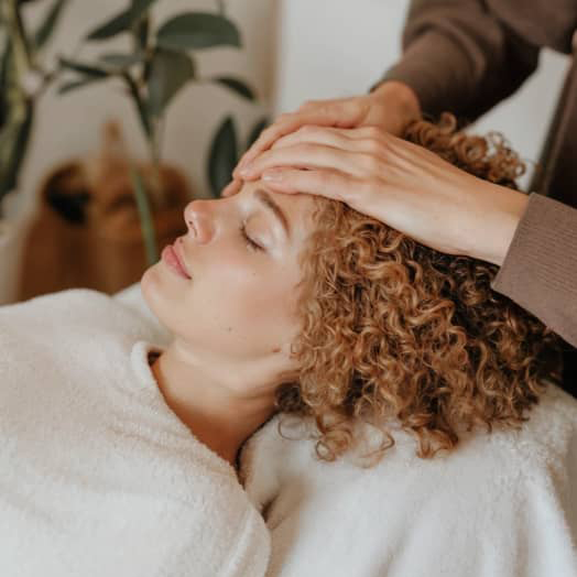 Woman with curly hair lying back and receiving a head massage in a relaxing setting.