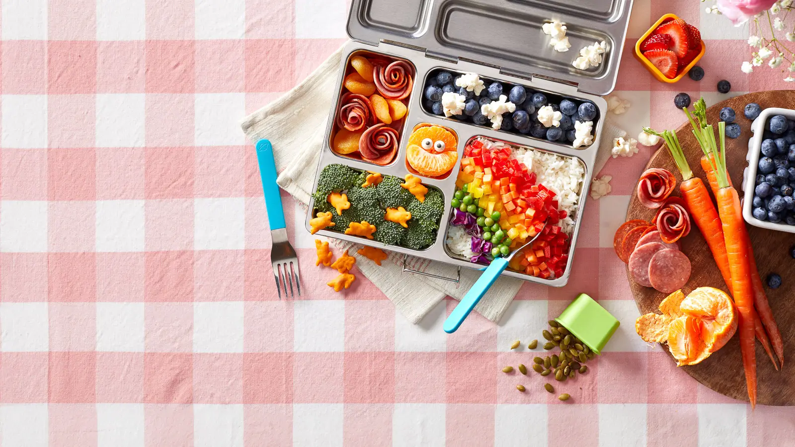 Top-down view of a colorful children's lunchbox meal, creating a vibrant spring. Image showcases nutritious and visually appealing meal prep options for kids, perfect for school lunches or picnics in the sunny weather.