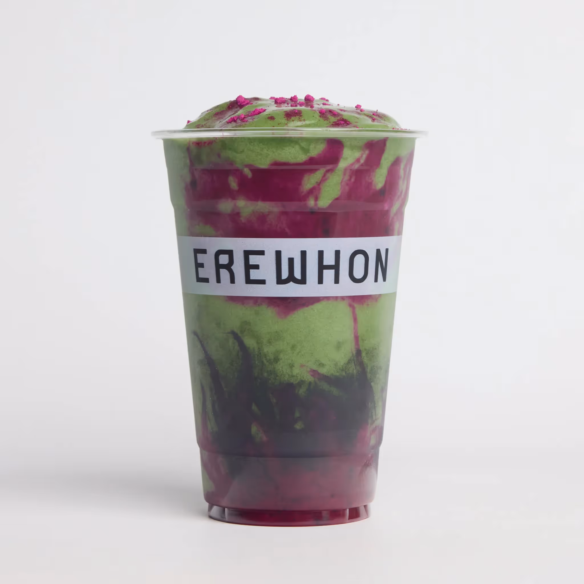 Erewhon branded smoothie cup with a green and purple swirl blend topped with crushed freeze-dried fruit, photographed against a light grey background