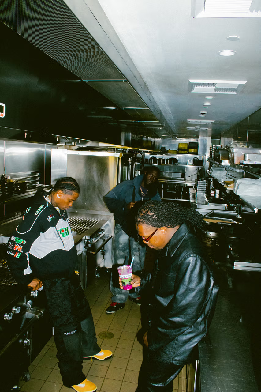Travis Scott and two others in a commercial kitchen holding Erewhon branded smoothie cups during the Storm Smoothie collaboration shoot