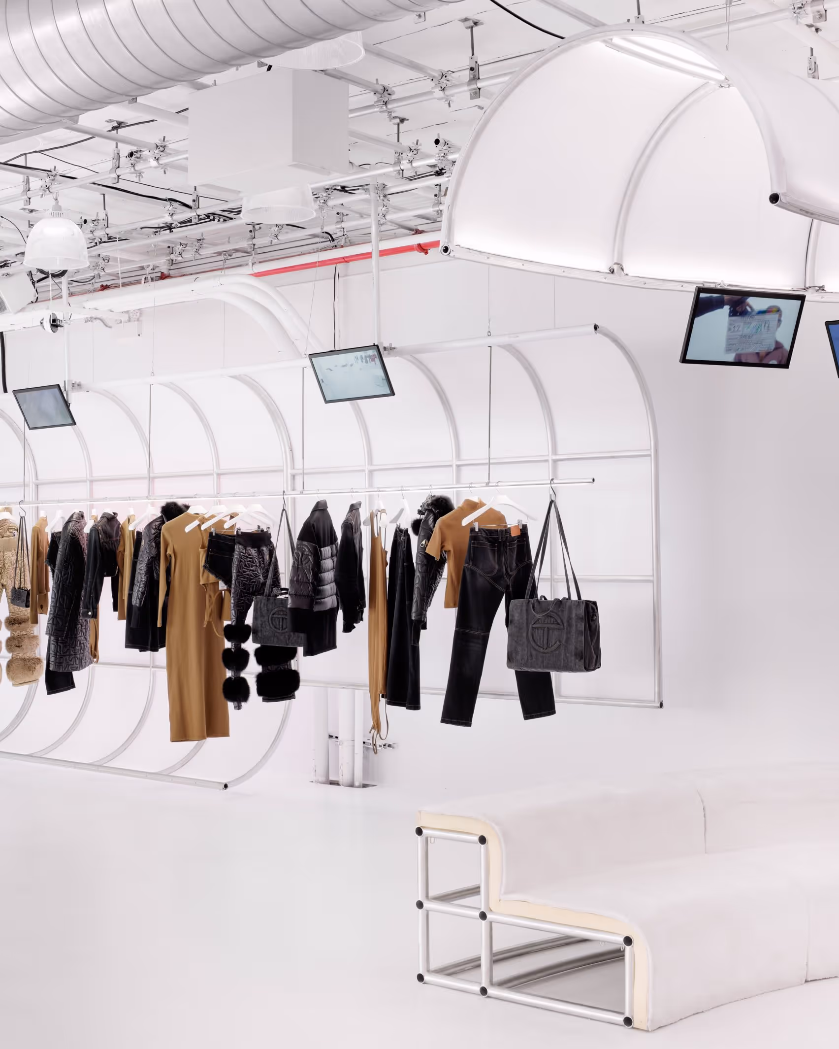 Interior of the Telfar flagship store in New York City showing white arched clothing racks with garments and shopping bags displayed against an all-white industrial space