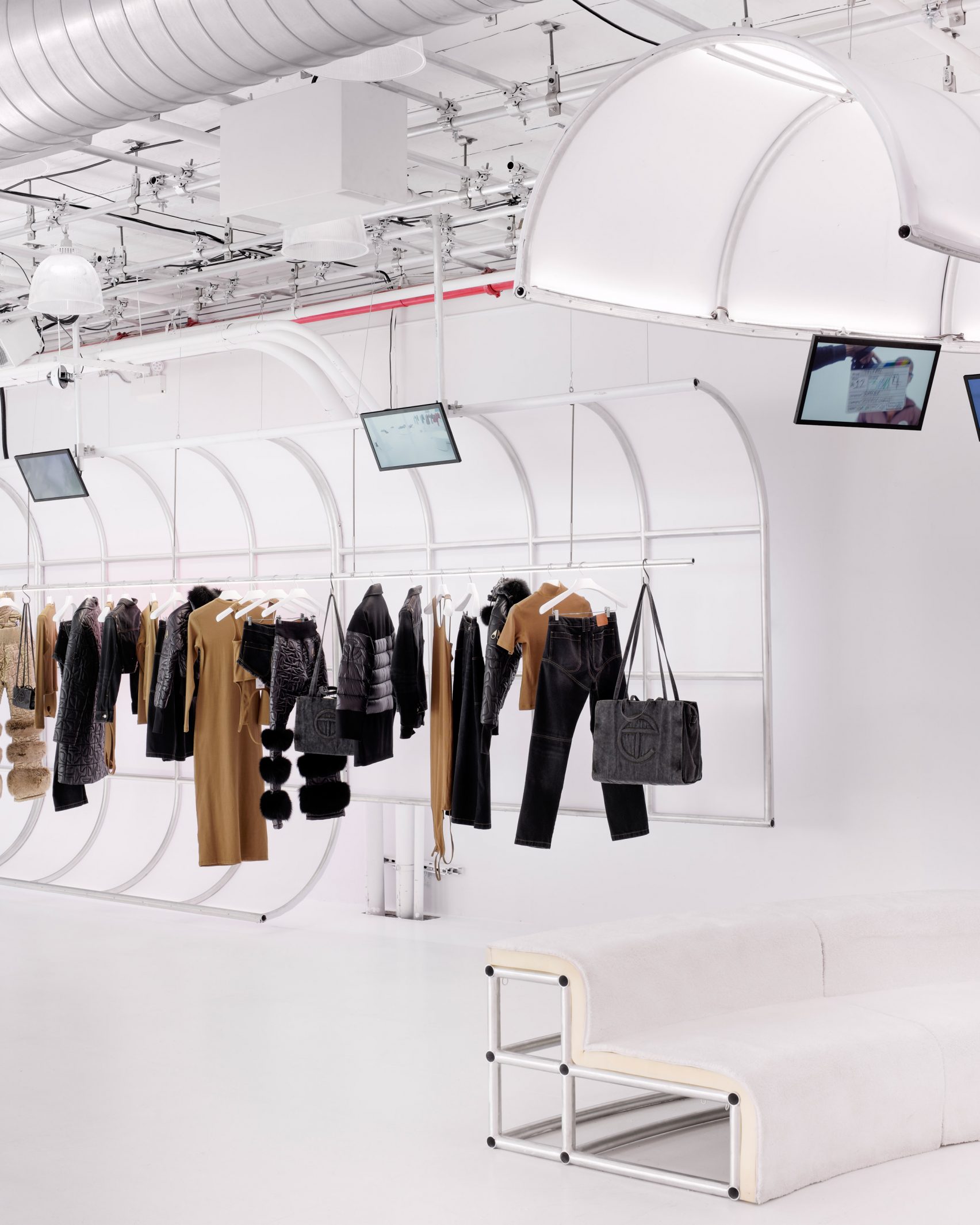 Interior of the Telfar flagship store in New York City showing white arched clothing racks with garments and shopping bags displayed against an all-white industrial space