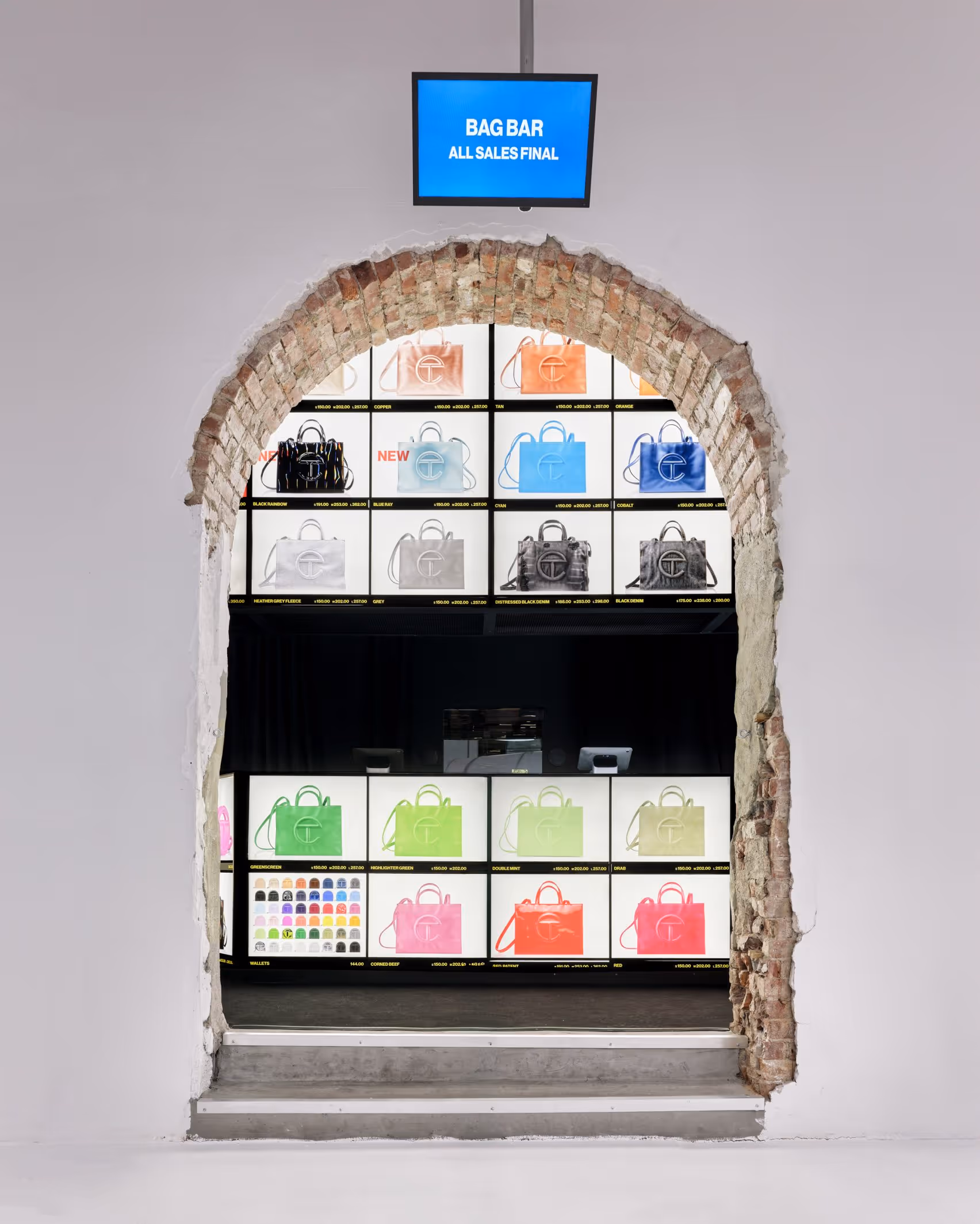 Telfar's Bag Bar display inside the NYC flagship store, showing the full range of Shopping Bags in multiple colorways on backlit shelves framed by an exposed brick archway