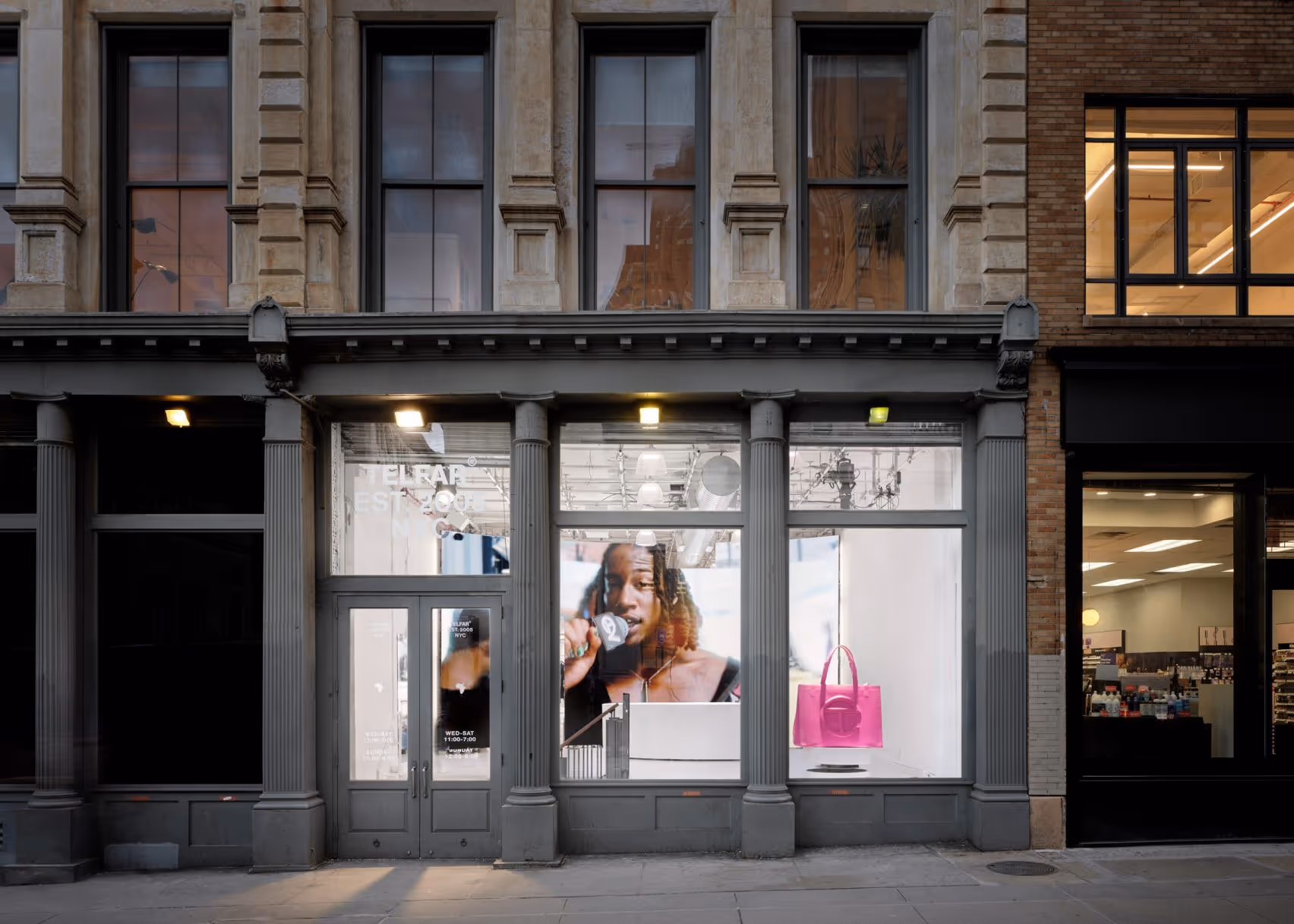 Exterior facade of the Telfar flagship store at 408 Broadway in New York City, with storefront windows displaying a large campaign portrait and a pink Telfar Shopping Bag