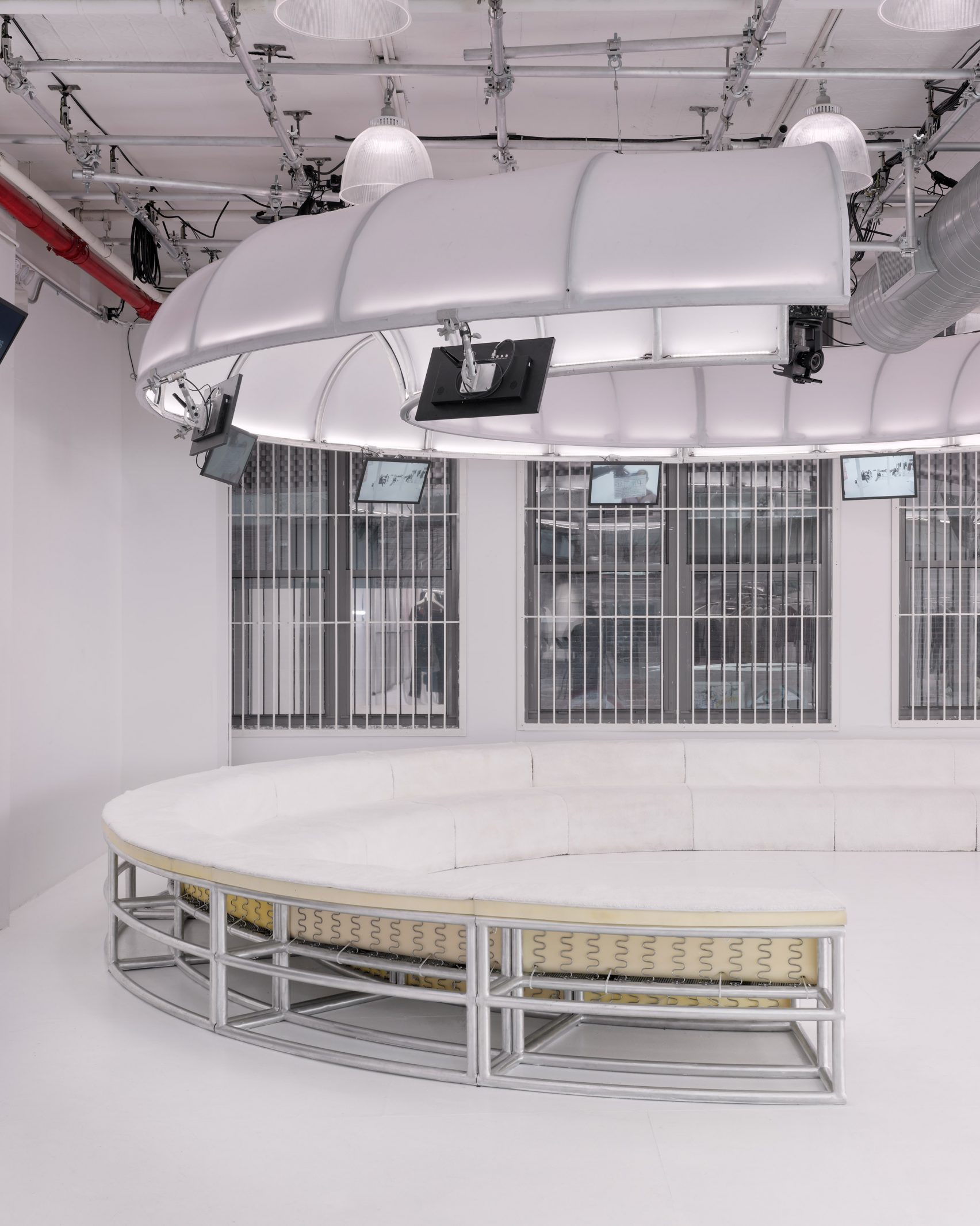 Circular white upholstered seating area with aluminium frame inside the Telfar flagship store in New York City, surrounded by arched white ceiling structures and suspended monitors