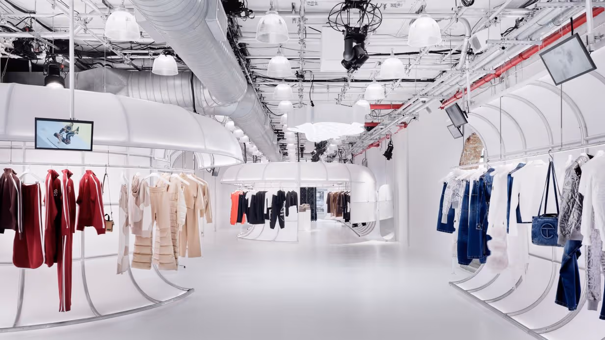 Wide-angle view of the Telfar flagship store interior at 408 Broadway NYC, showing curved aluminium clothing racks with full ready-to-wear collection displayed across the all-white industrial space