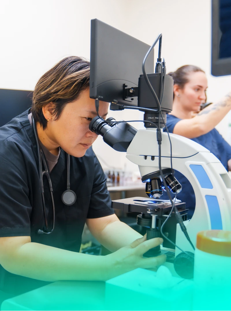 Woman looking through microscope in a medical setting.