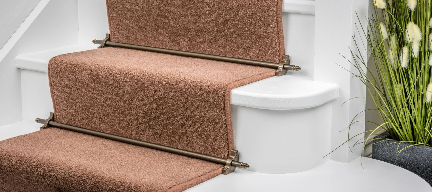 Close-up of brown carpet runner secured on white stairs with decorative bronze stair rods.