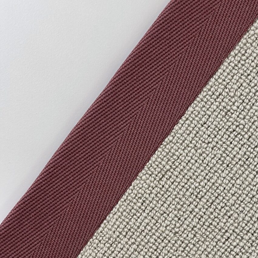 Close-up of carpet edging tape in dark red woven fabric next to a beige textured carpet.