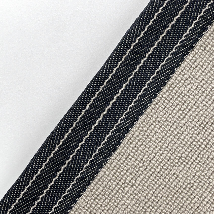 Close-up of a beige woven carpet with a black and white striped binding tape along the edge.
