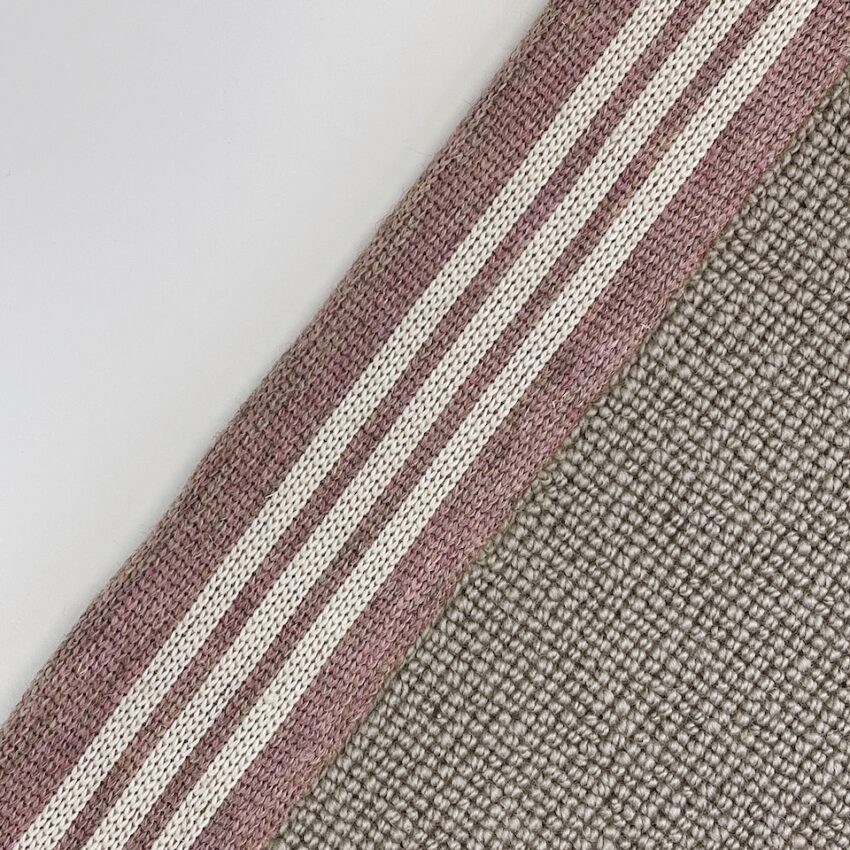 Close-up of woven carpet edging tape in pink and white stripes alongside a textured beige carpet.
