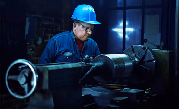 Worker in protective gear operating a machine in a workshop.