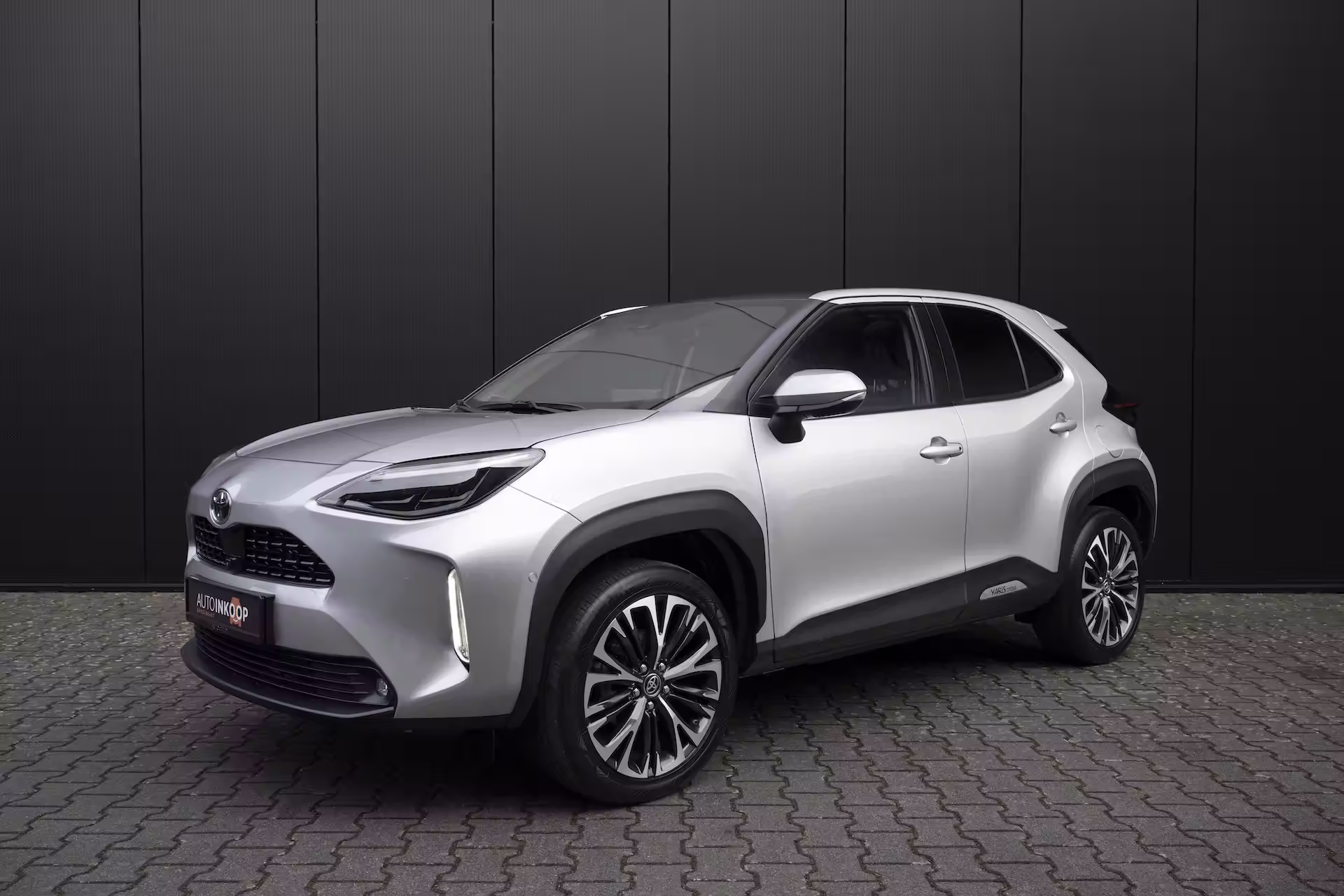 Zilverkleurige Toyota Yaris Cross SUV geparkeerd voor een zwarte achtergrond.