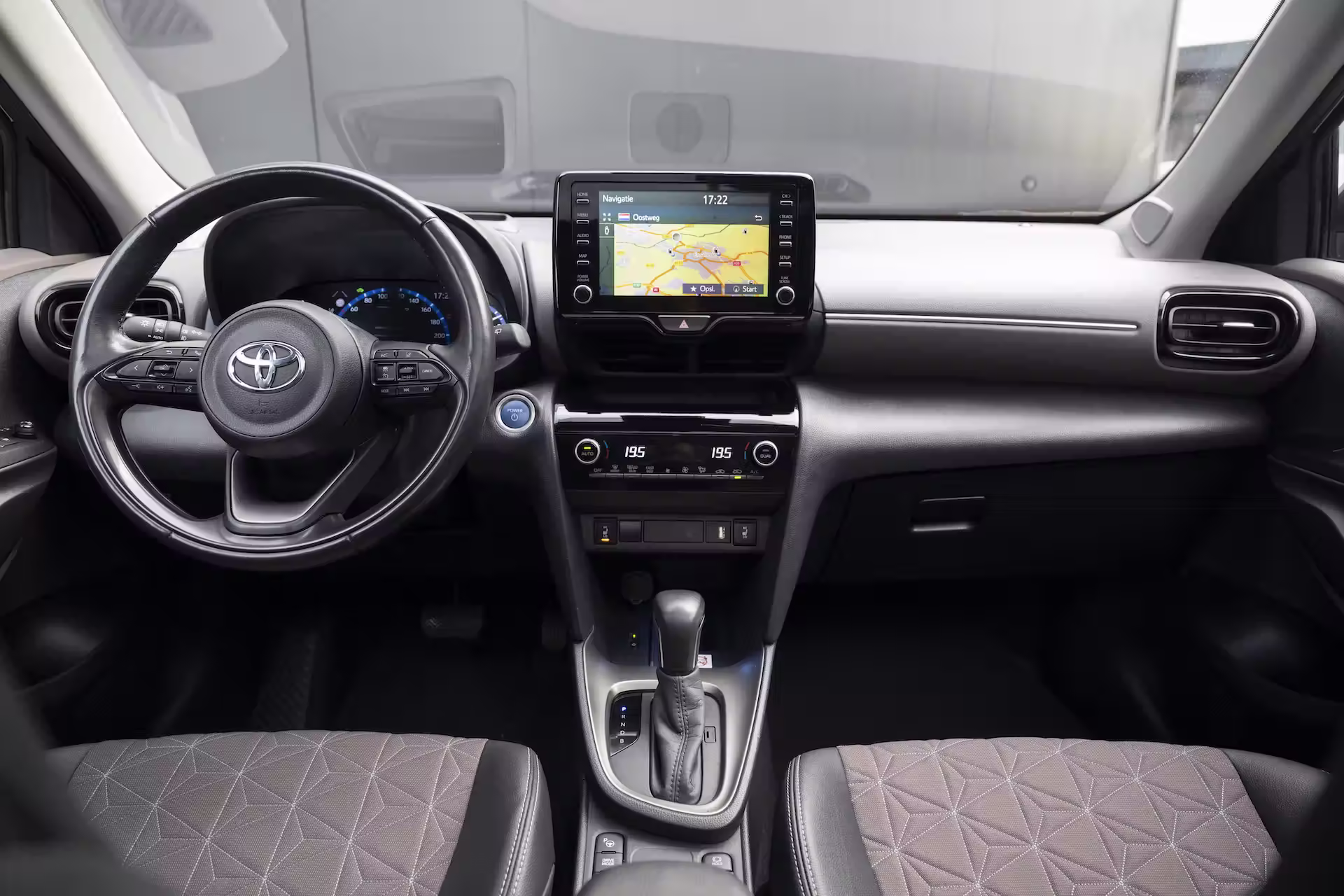 Interieur van een Toyota-auto met een stuurwiel, navigatiescherm, automatische versnellingsbak en stoffen voorstoelen.