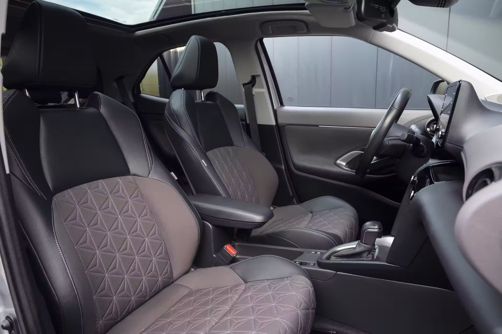 Interieur van een moderne auto met zwart-grijze stoffen en lederen voorstoelen en een panoramadak.