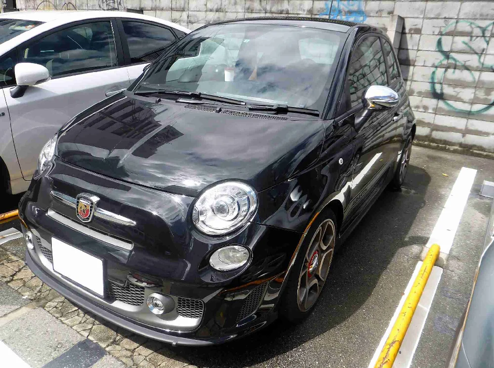 Zijaanzicht van een grijze Abarth 595 op een parkeerplaats.