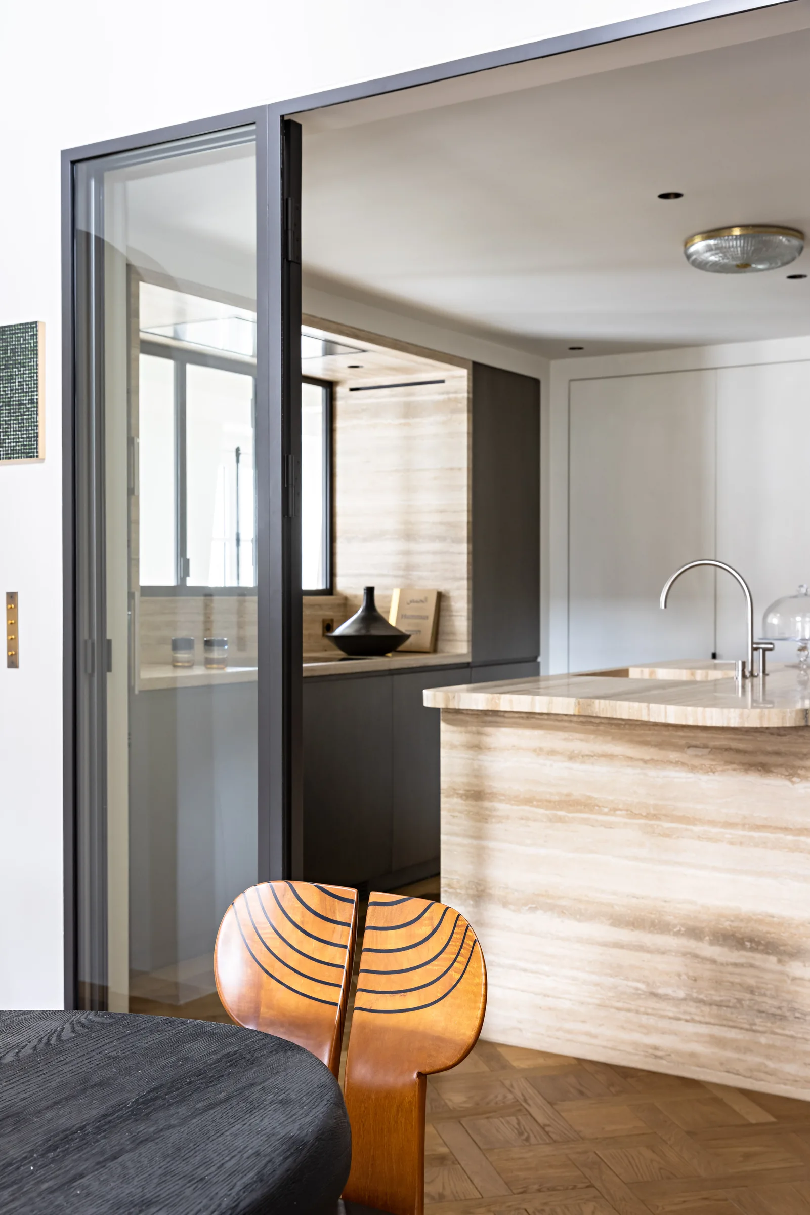 Cuisine en travertin vue à travers une verrière en acier, rénovation d'appartement à Saint-Germain, Paris