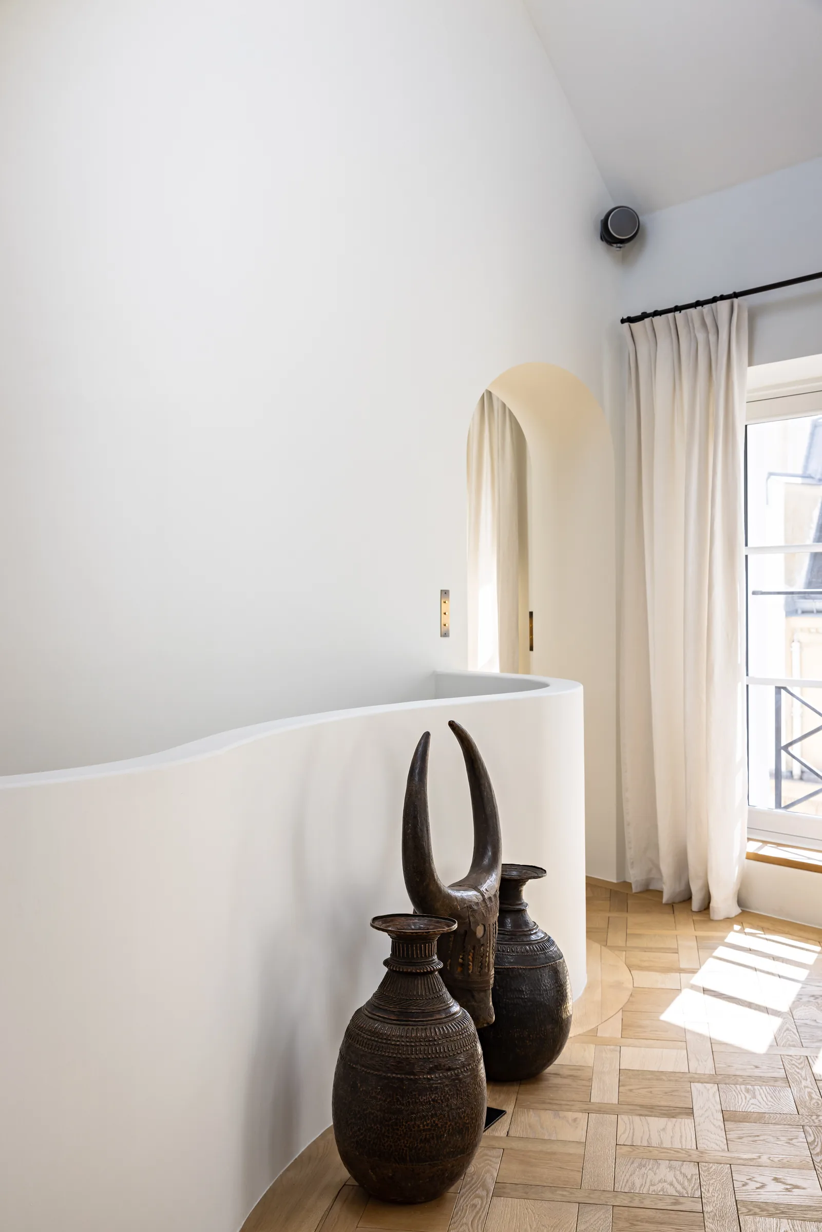 Palier épuré avec vases décoratifs et fenêtre cintrée, appartement haussmannien rénové Saint-Germain, Paris