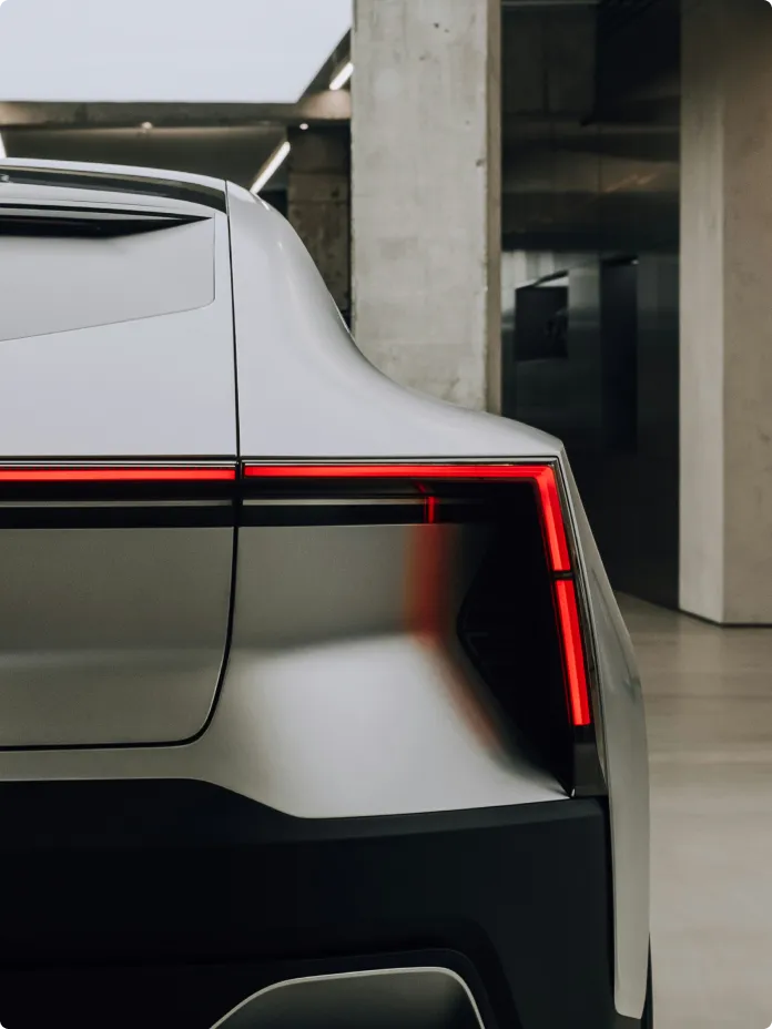 A futuristic car's rear end is displayed inside a modern building, showcasing sleek design and advanced technology.