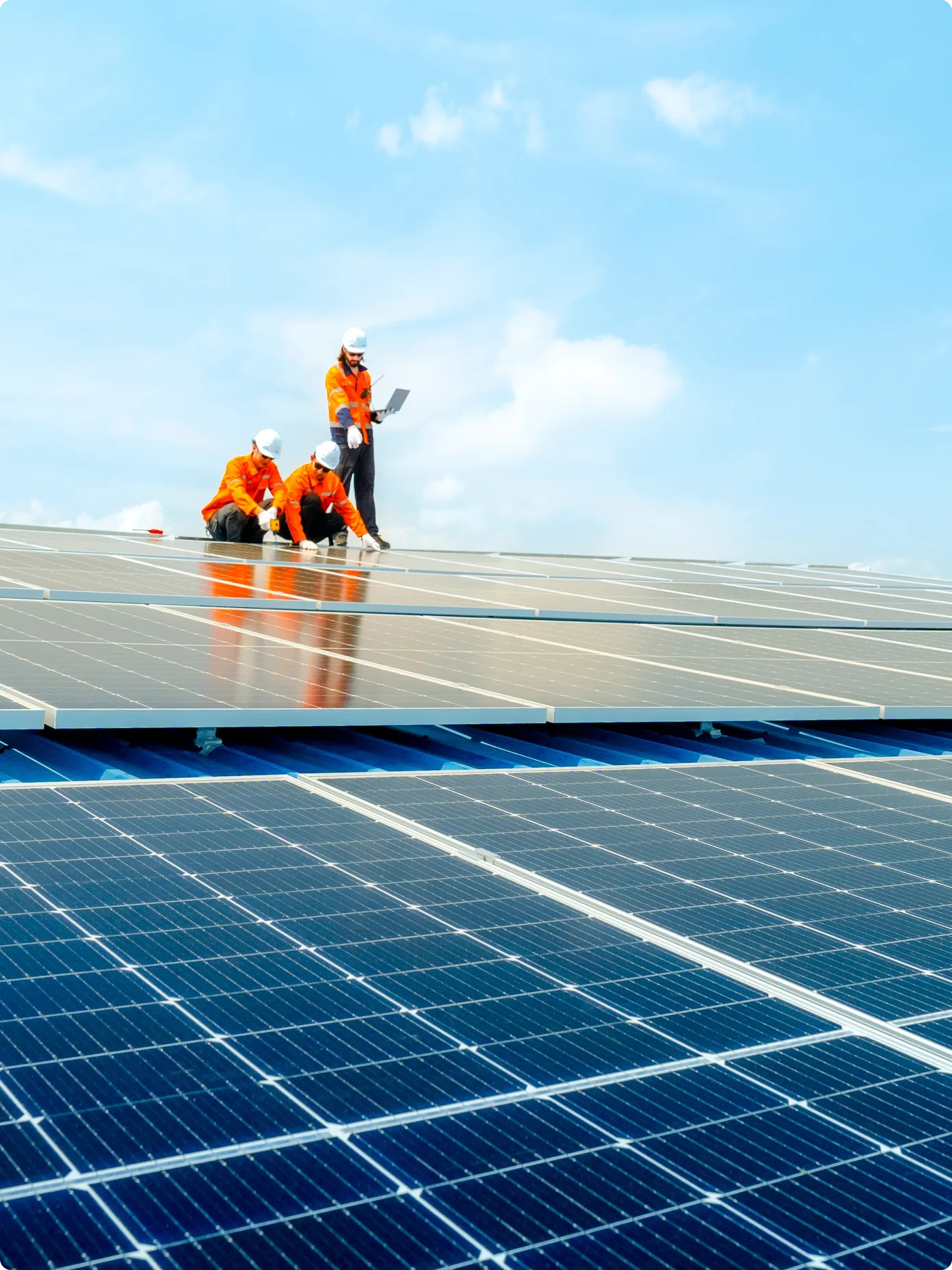 Three workers installing solar panels on a rooftop, wearing safety gear and collaborating on the project.