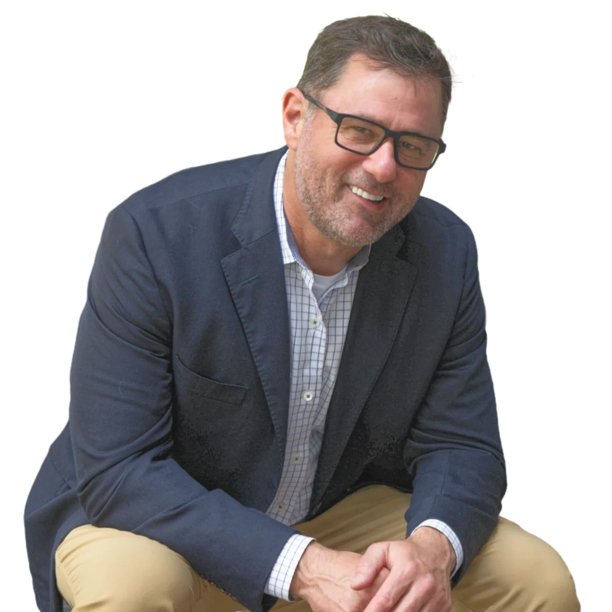 Smiling Data Coach Gravy wearing glasses, navy blazer, checked shirt, and khaki trousers, sitting with hands clasped together. 1:1 ratio