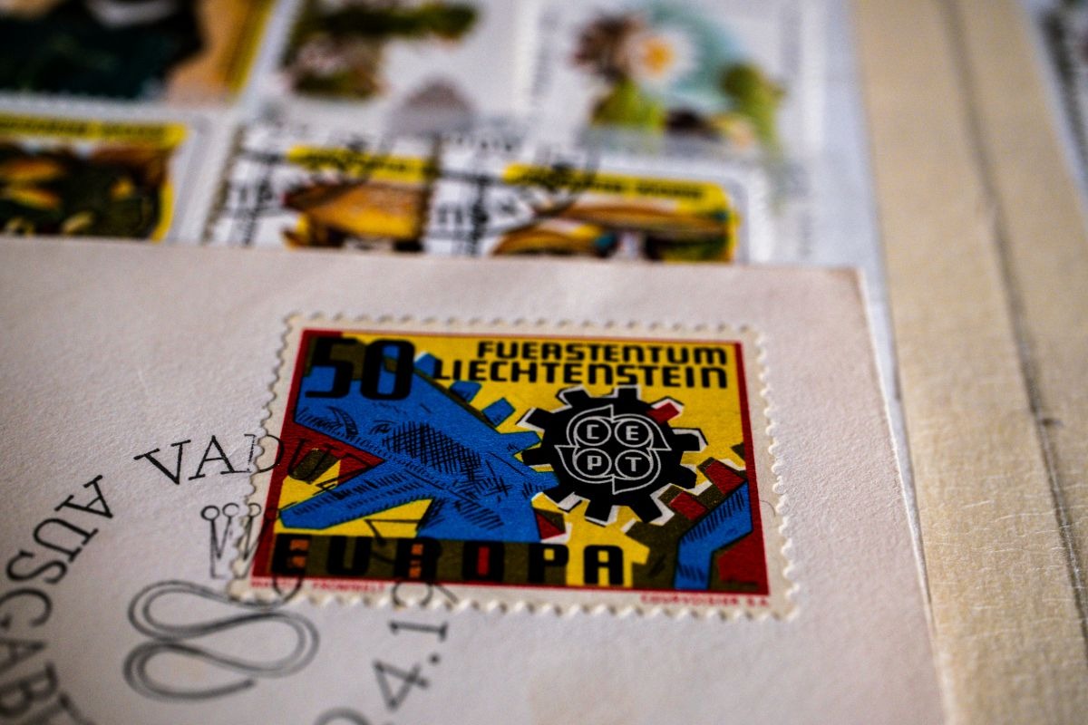 Briefmarke aus Liechtenstein auf einem Umschlag, Symbol für klassisches Porto im Vergleich zu modernem Online Frankieren.