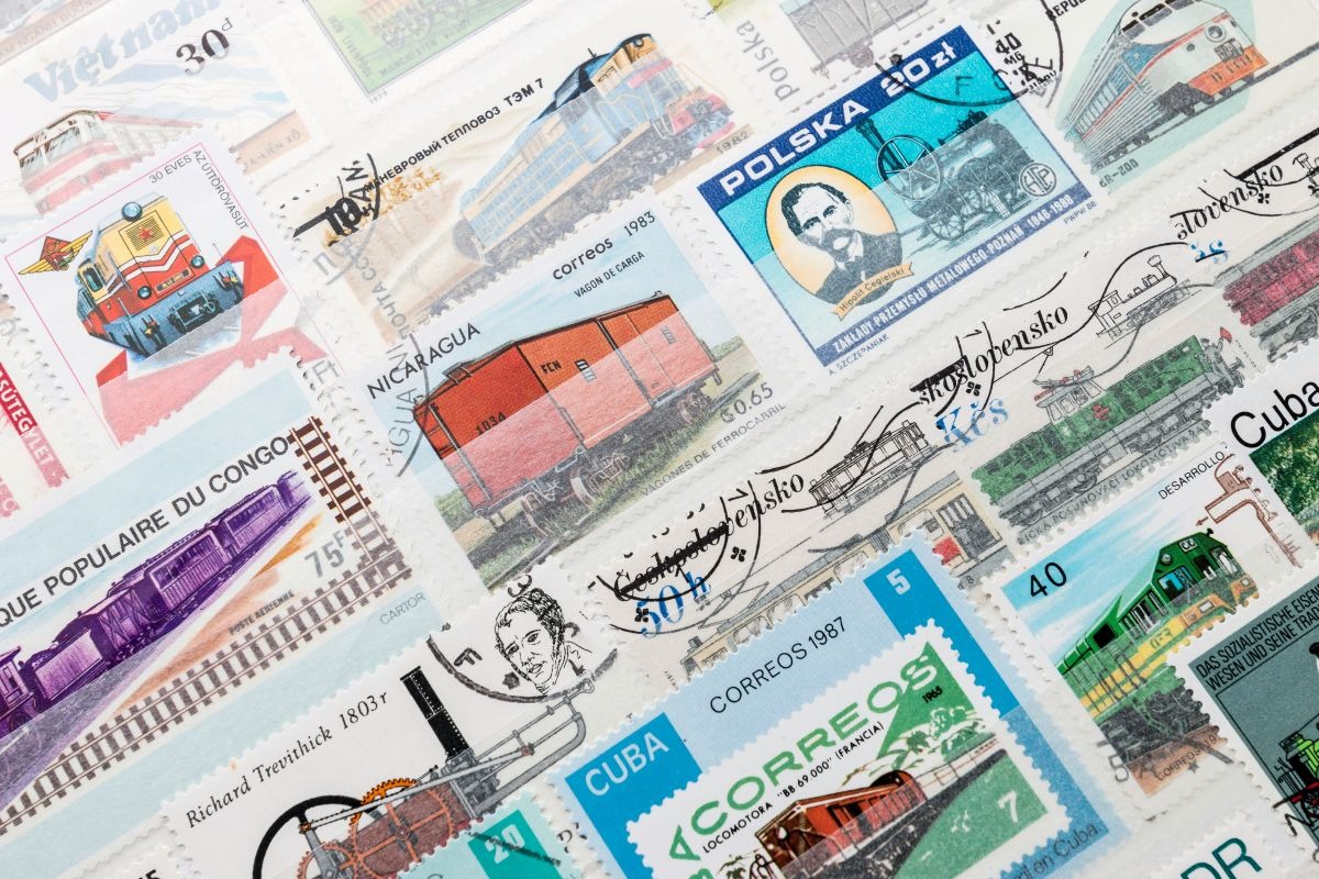 Sammlung internationaler Briefmarken mit Motiven von Zügen und Post, nostalgischer Kontrast zum Online Frankieren moderner Briefe.
