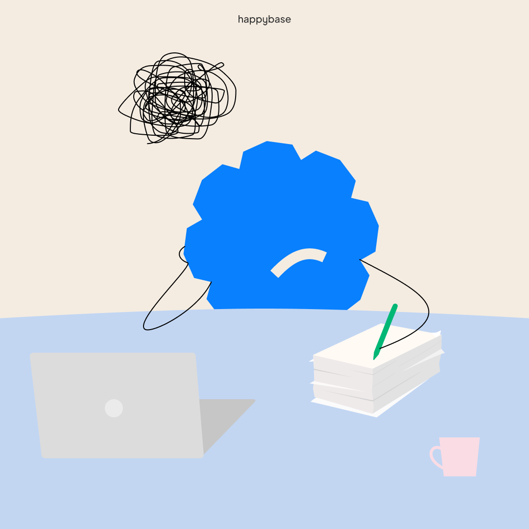 Illustration of a frustrated blue gear-shaped character with scribble above its head, sitting at a desk with a laptop, stacked papers, a green pen, and a pink cup.