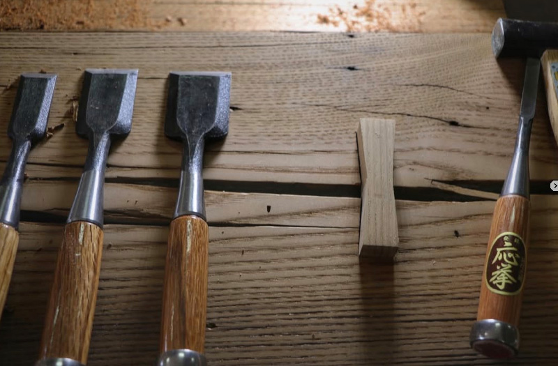 Image of chisels lined up on top of a dovetailed piece of wood.