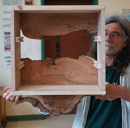 A man with glasses holding a custom, live-edge shelf