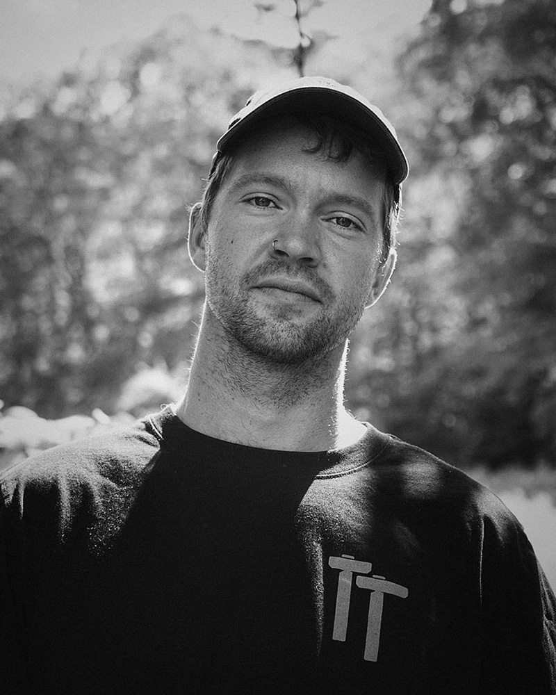 Black and white portrait of Justin Sechrest. Trees behind.