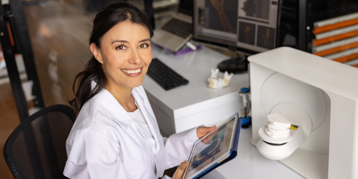 dentist poses for a picture next to a dental mold in a machine