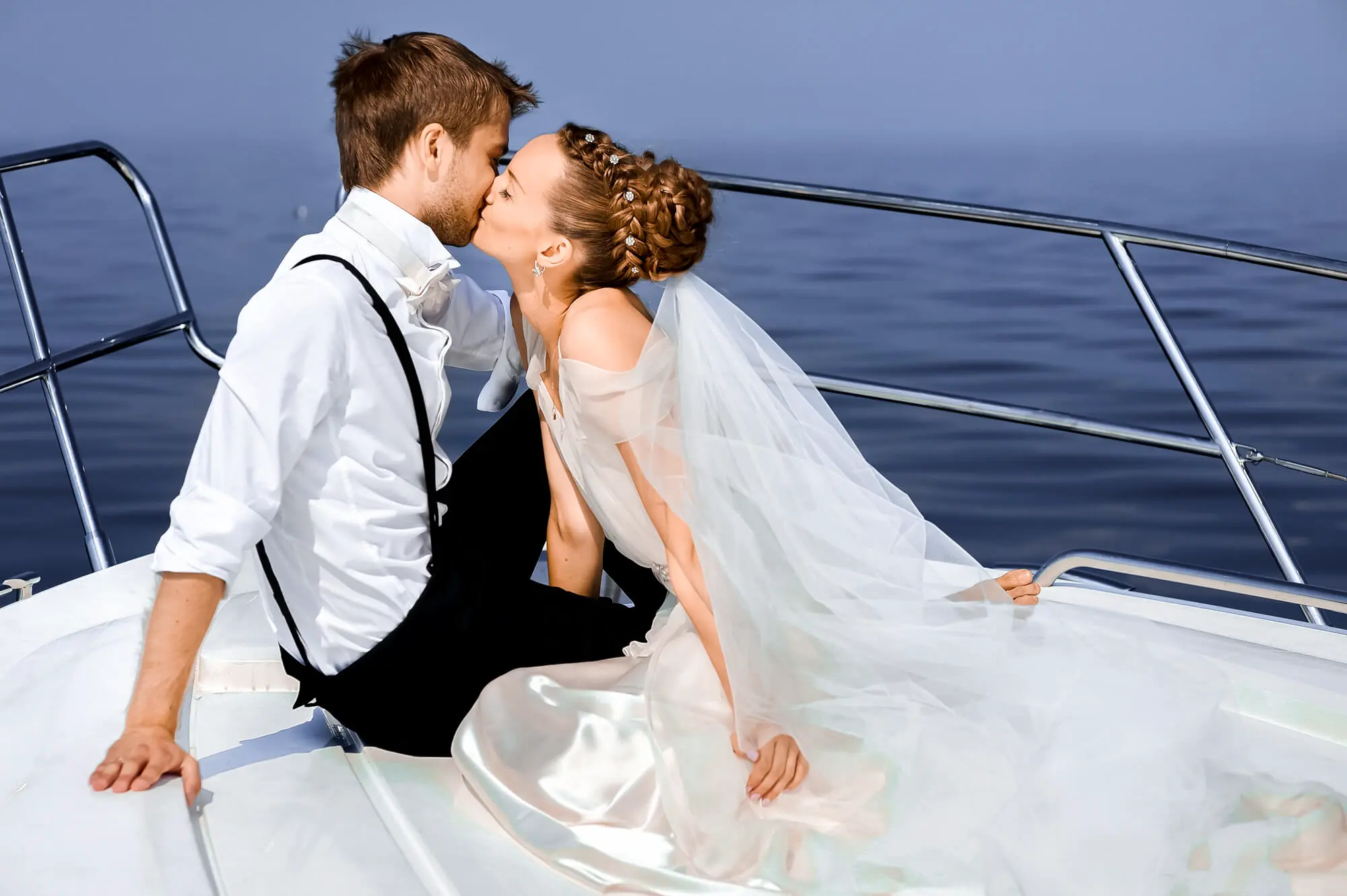 A young married couple, dressed as bride and groom kissing each other on private yacht during their honeymoon.