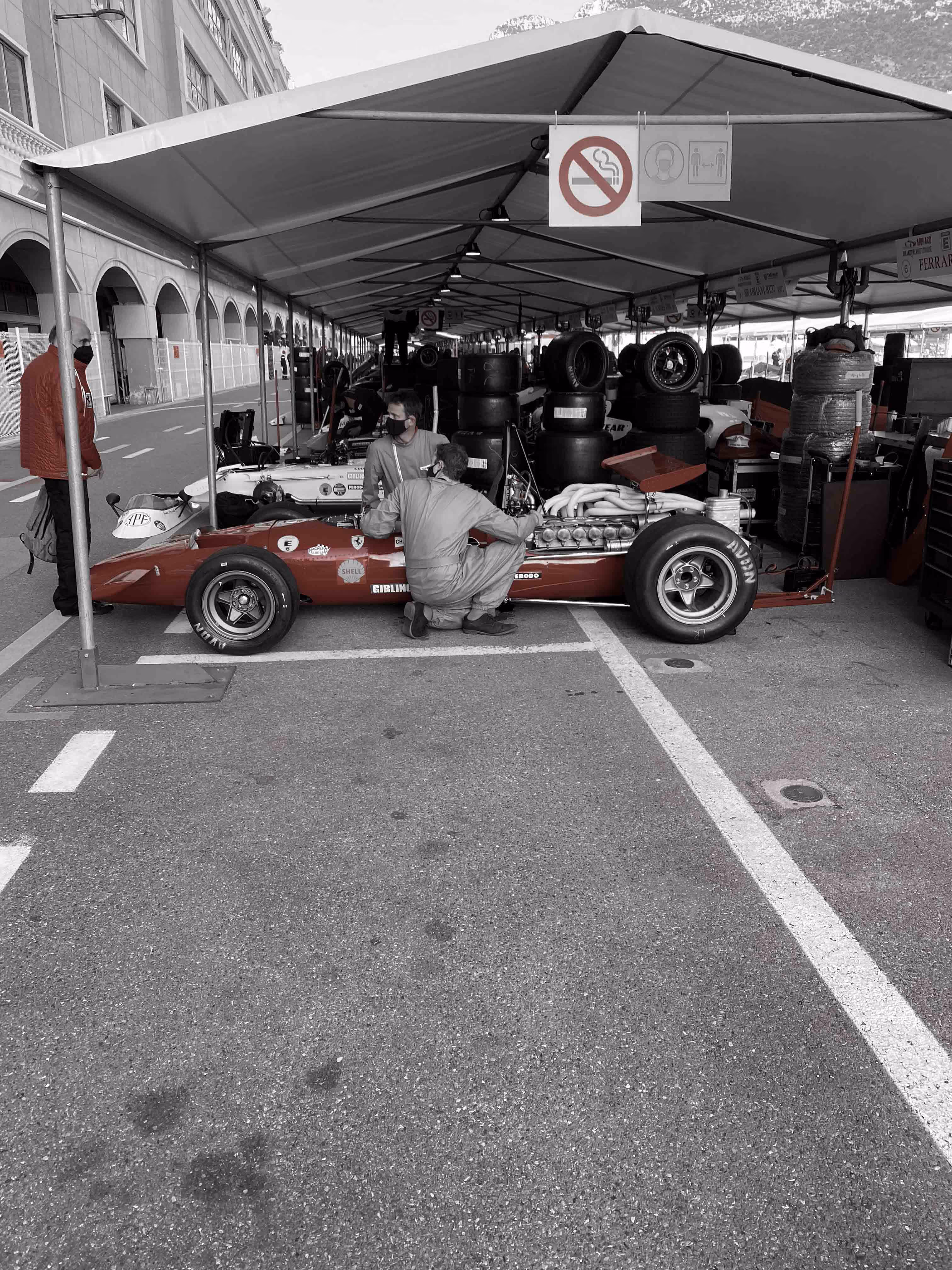 Mechanic working on historic red race car in paddock area.
