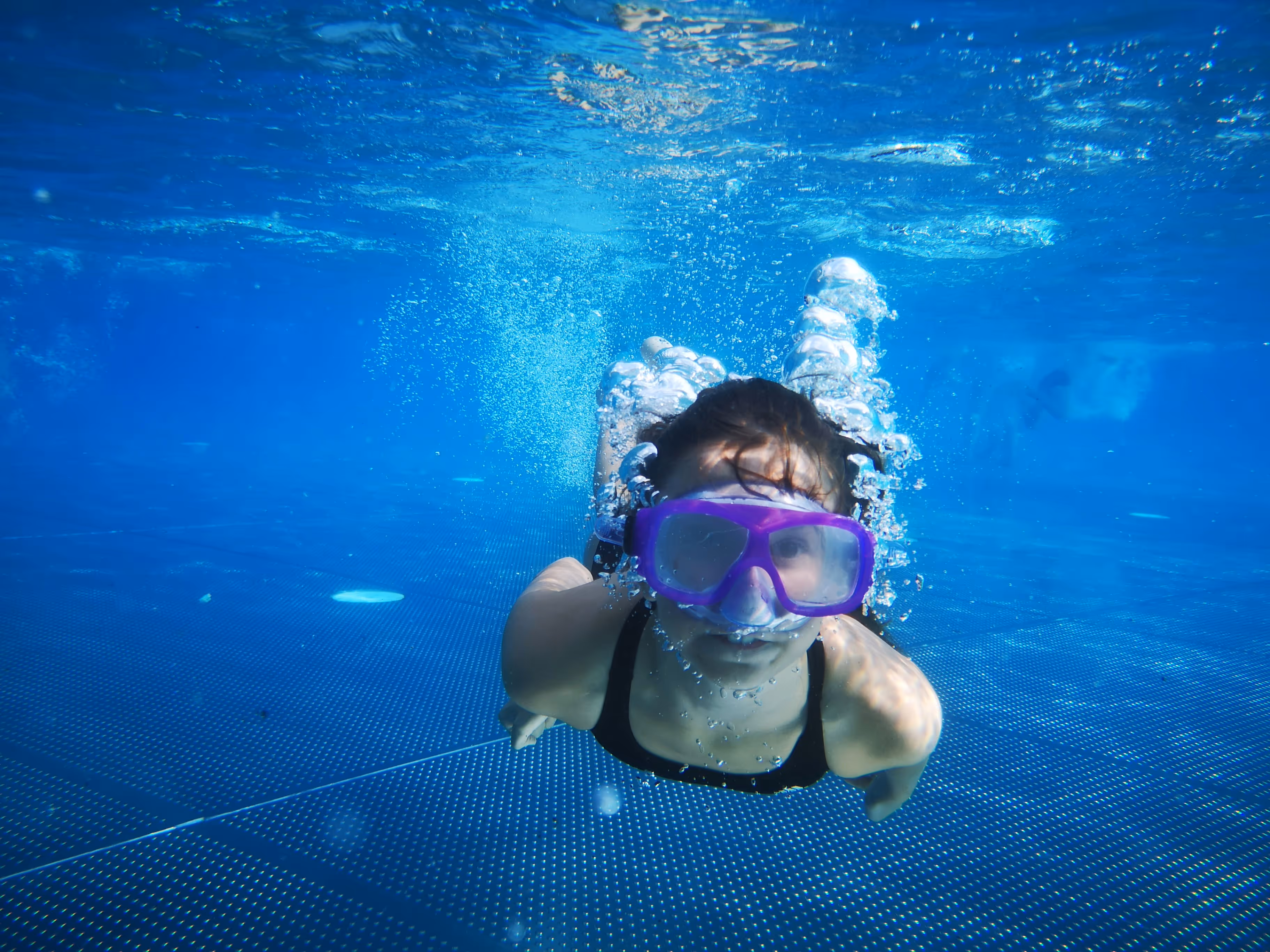 Girl swimming underwater with goggles.
