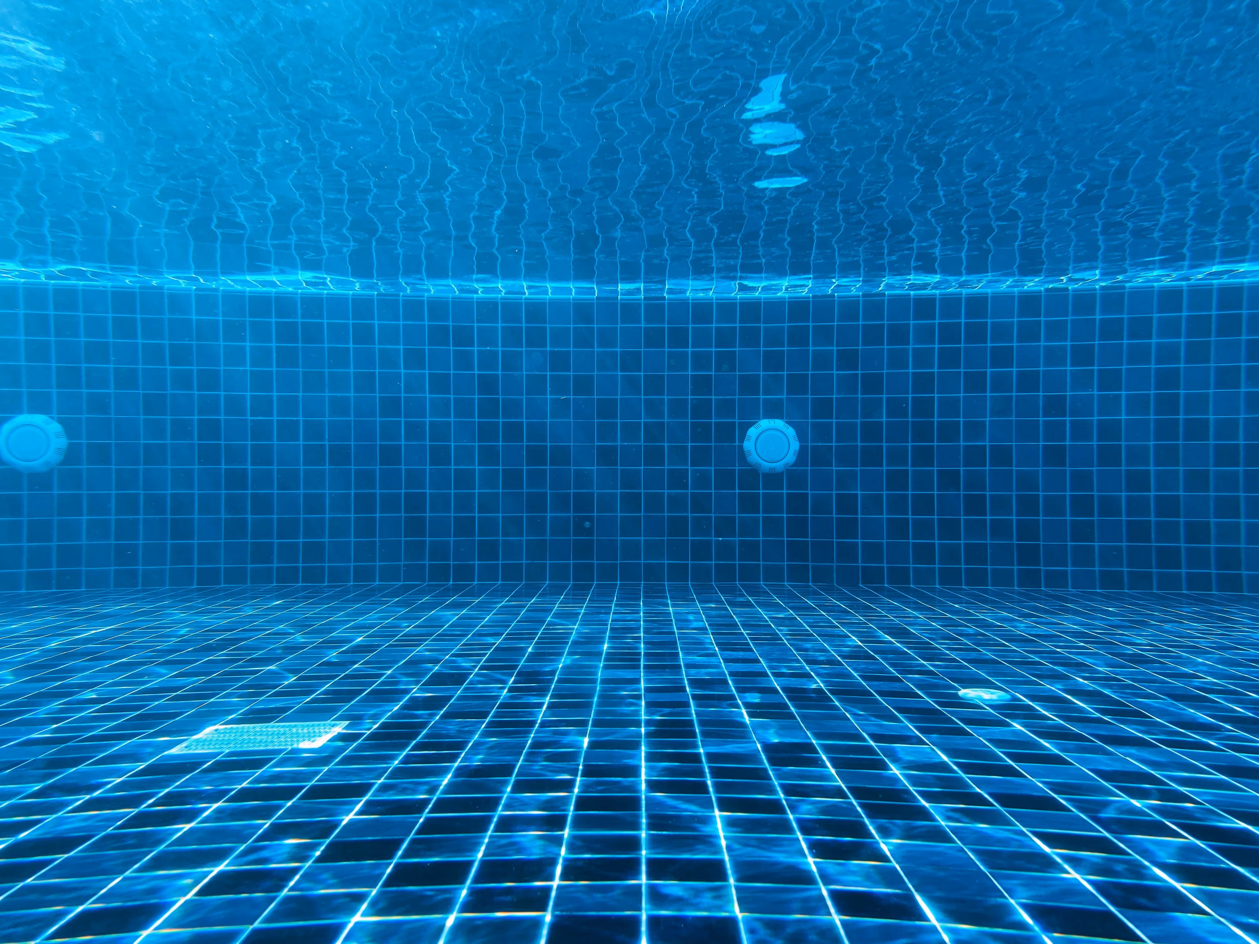 Empty swimming pool floor with blue tiles underwater.