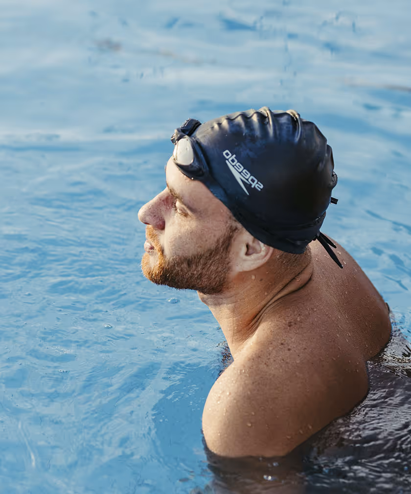 Man in swim cap and goggles resting in the pool.