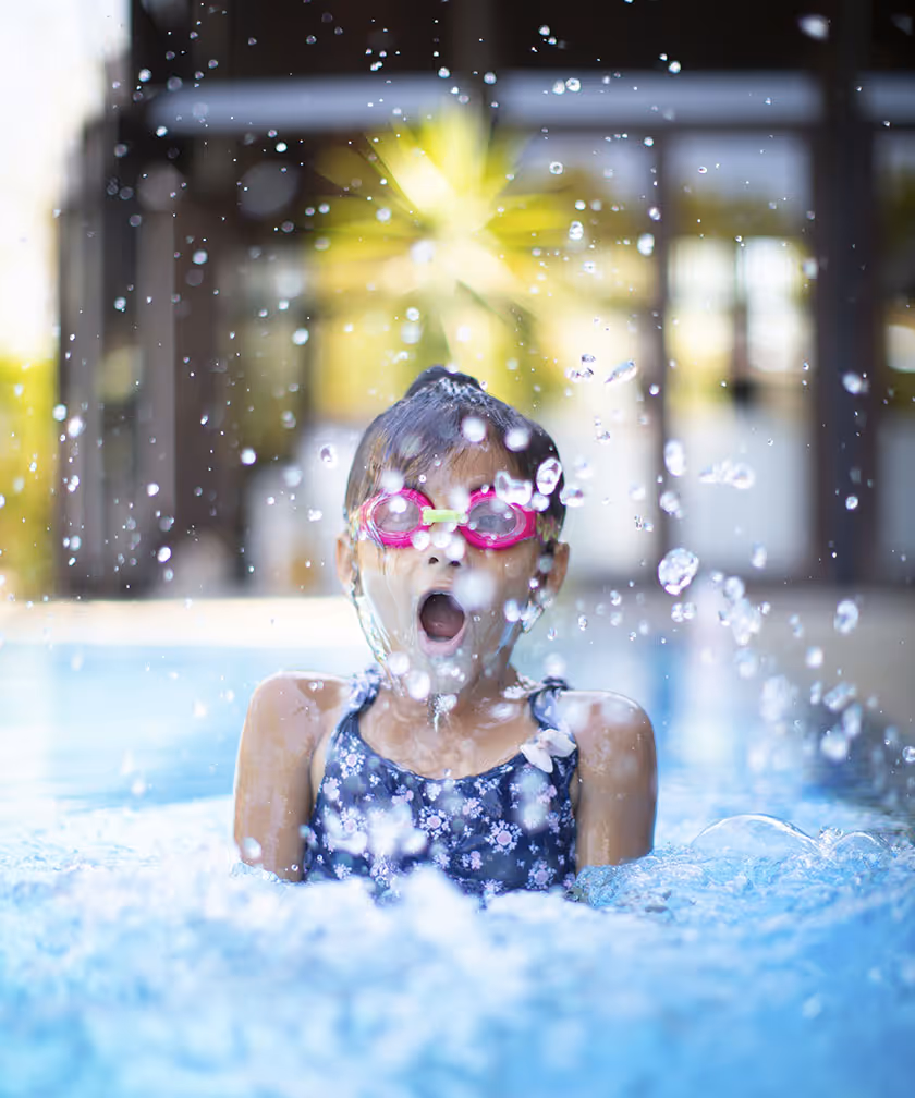 Girl splashing water while wearing goggles in a pool.