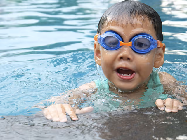 Toddler wearing blue goggles swimming at the pool edge.
