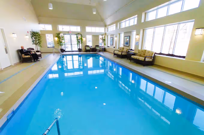 Indoor swimming pool with lounge chairs and large windows.