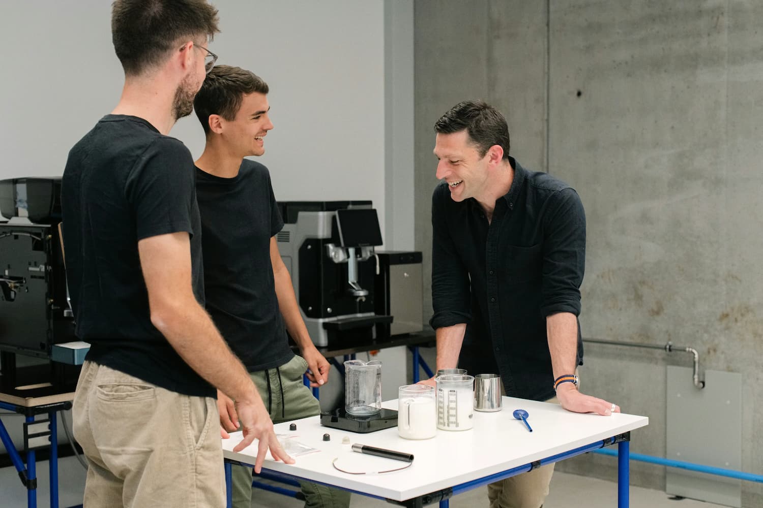 Three men smiling around a table with milk jugs.