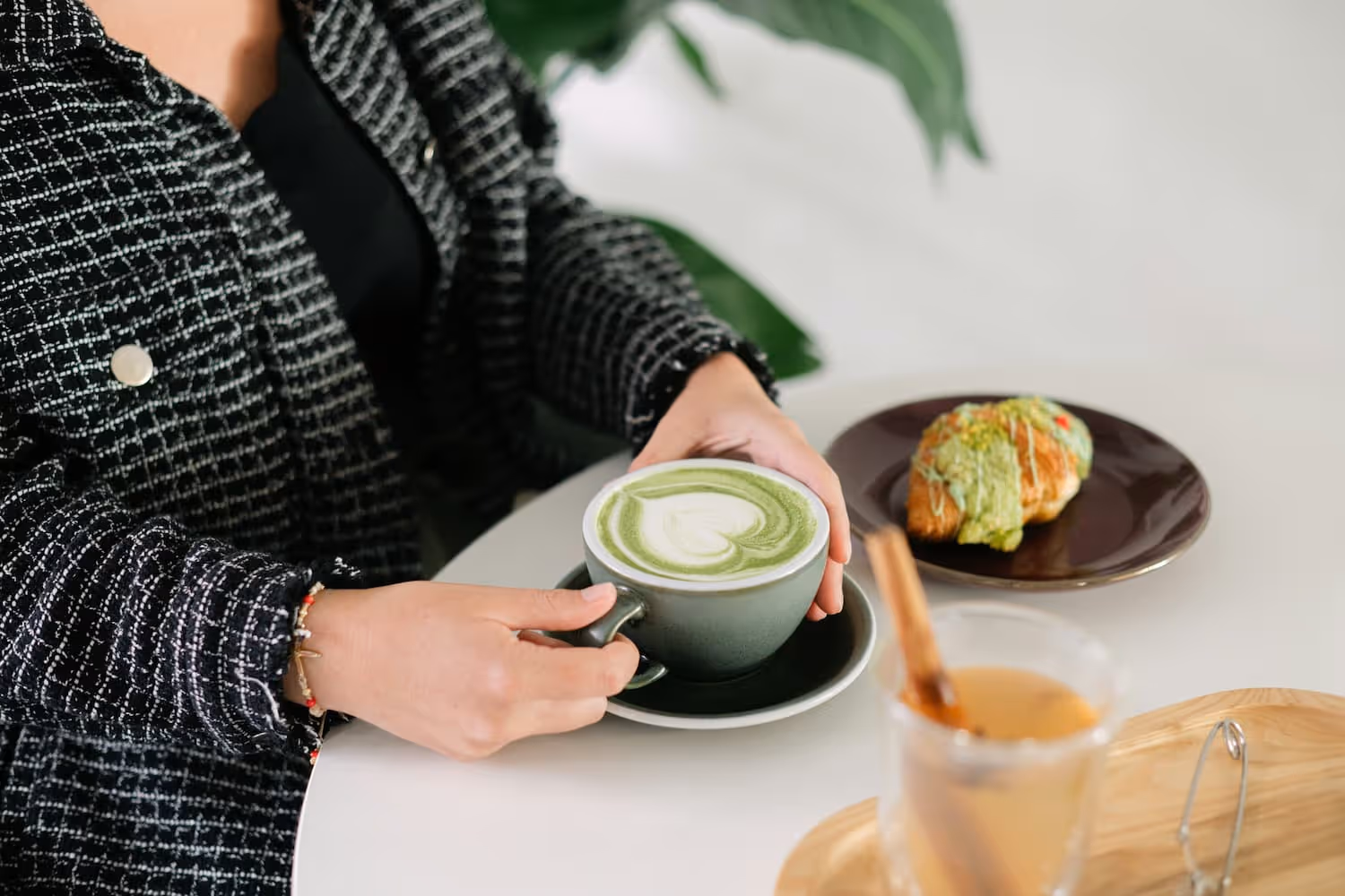 Hands holding a matcha latte on a table with a pastry. 