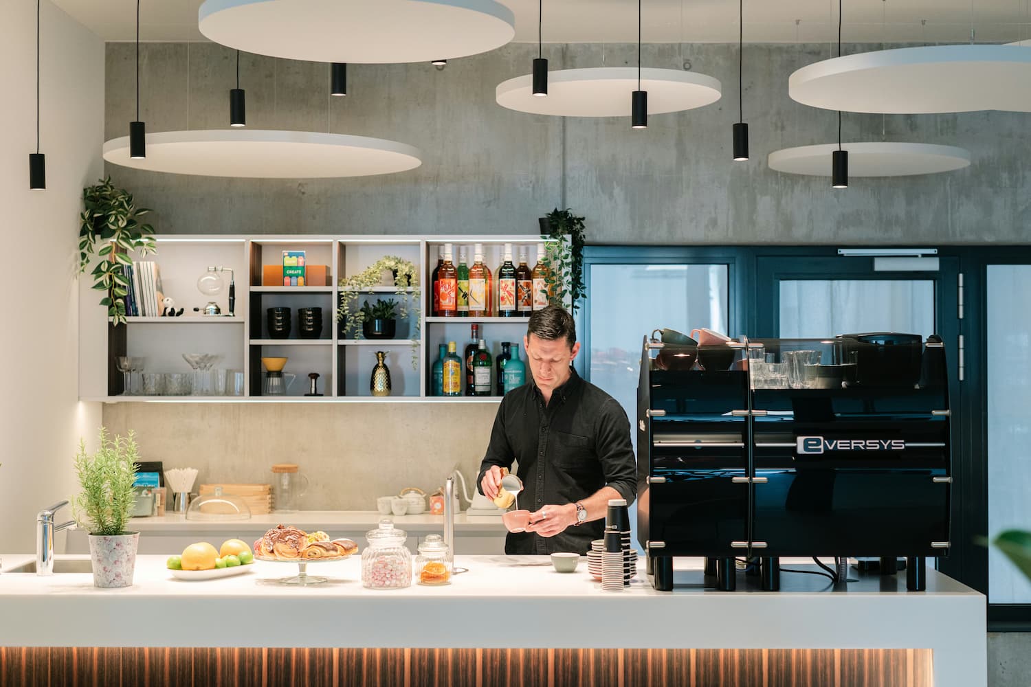 A man pouring milk into a cup behind a counter with a coffee machine.