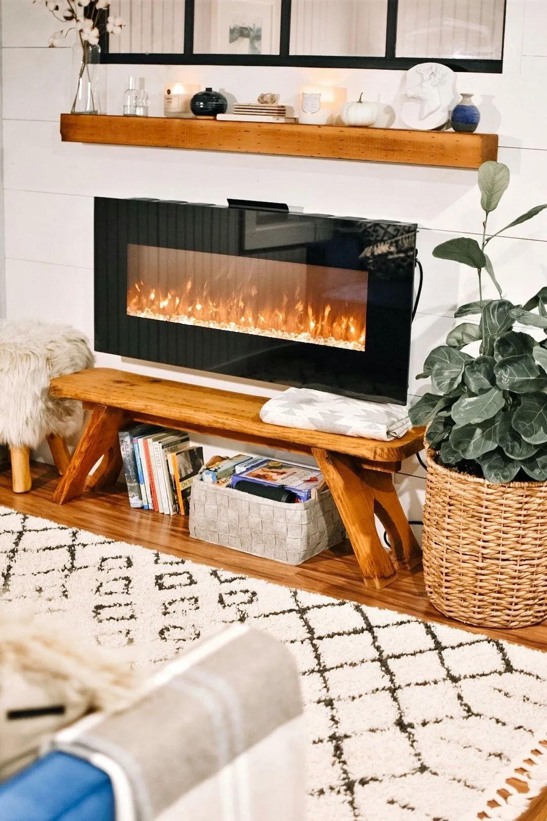 Cozy living room featuring a sleek electric fireplace, wooden bench, and decorative accents on a modern rug. 