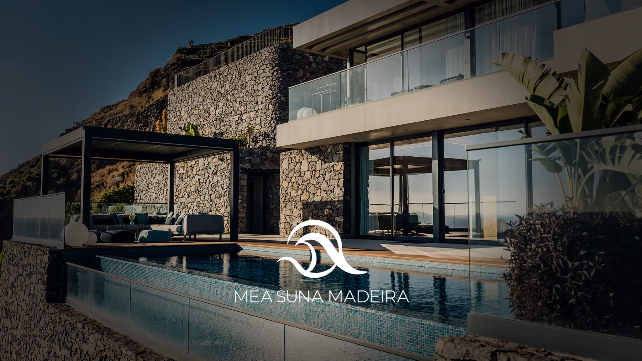 Modern house with stone walls, a glass balcony, a pool, and outdoor seating area under a pergola.