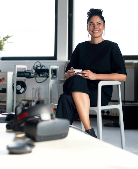 A smiling woman sits in a modern office, holding a cup of coffee