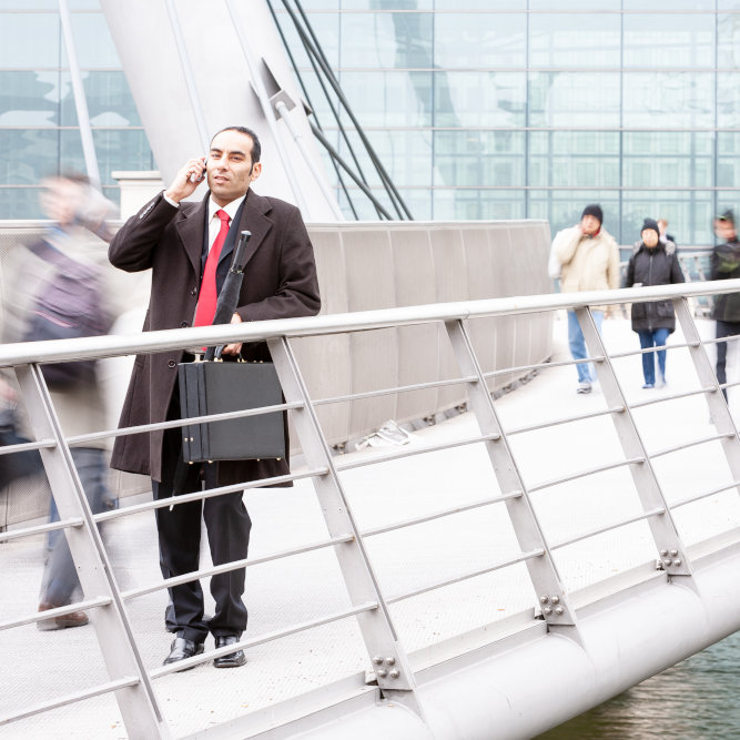 Business professional on phone call standing on modern walkway with people passing in background